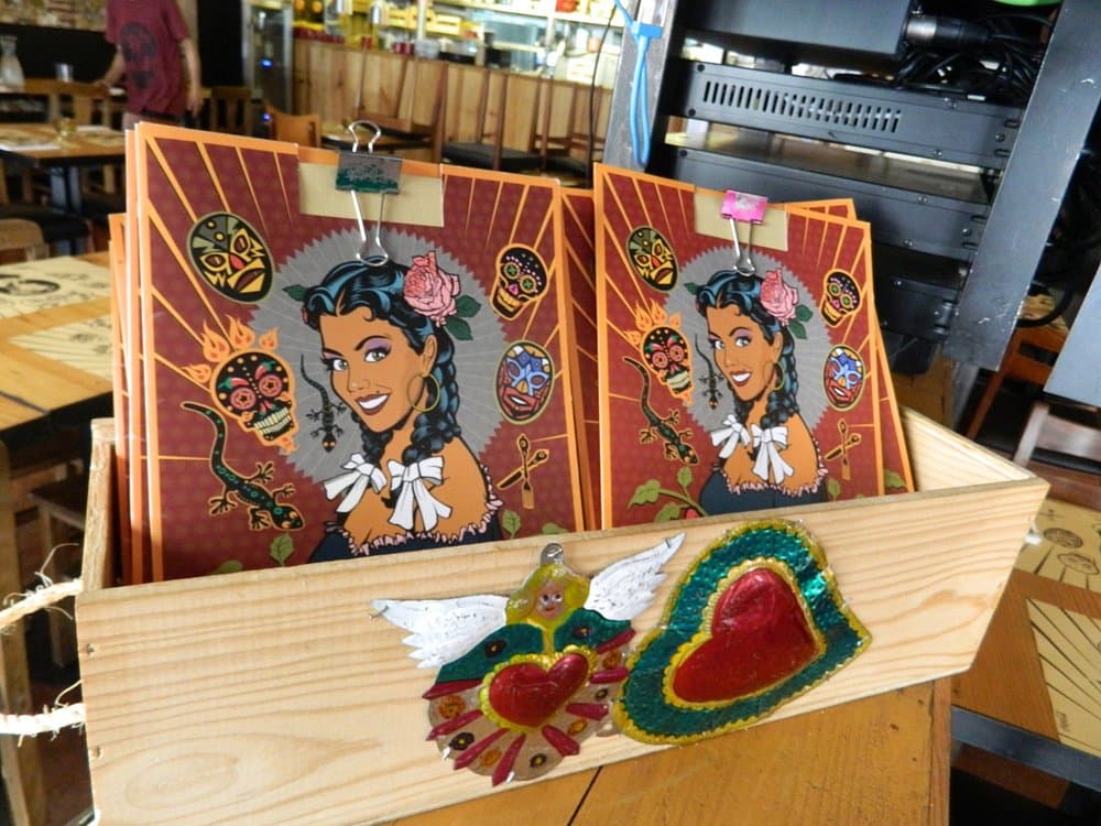 Printed menus with Las Ficheras artwork stacked in a wooden crate